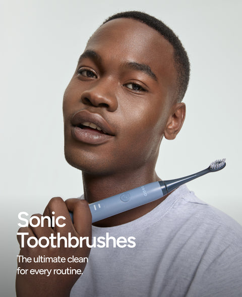Man holding a toothbrush against a grey background with text that says "Sonic Toothbrushes, The ultimate clean for every routine".